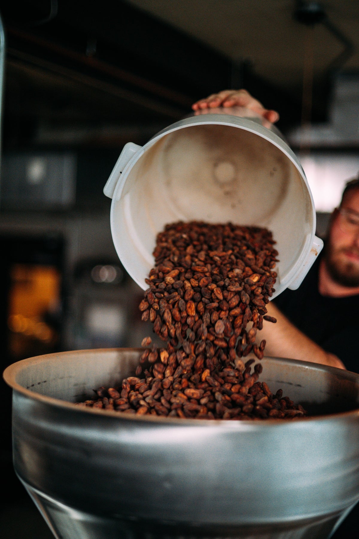 Olive and Sinclair employee dumping cocoa beans into chocolate making equipment 