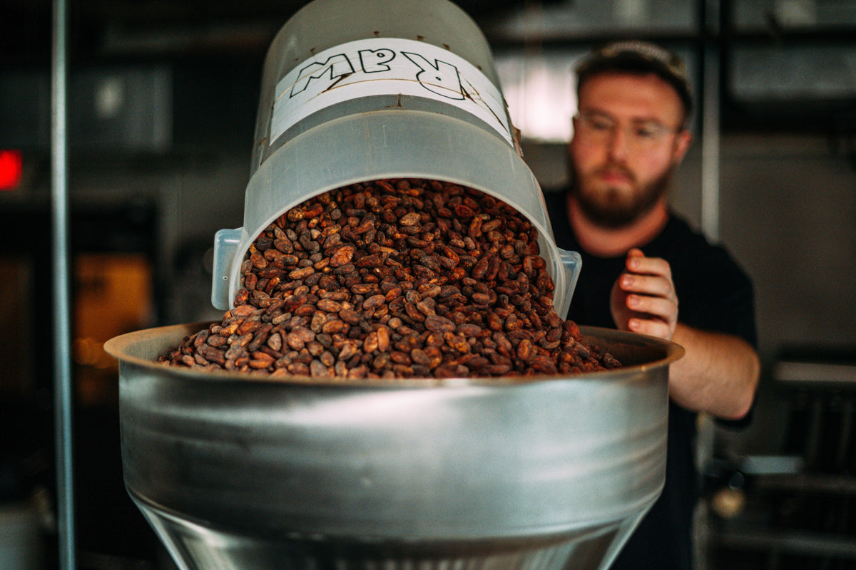 Person holding a metal funnel with cacao beans and 'RAW' label.